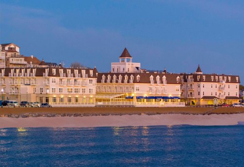 A coastal hotel illuminated at dusk, featuring a tower and multiple balconies along the sandy beach.