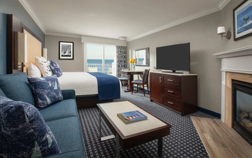 A modern hotel room featuring a bed, sofa, TV, and a view of the outdoors through large windows.