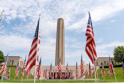 A tall monument surrounded by American flags on a sunny day, with people gathered at its base.
