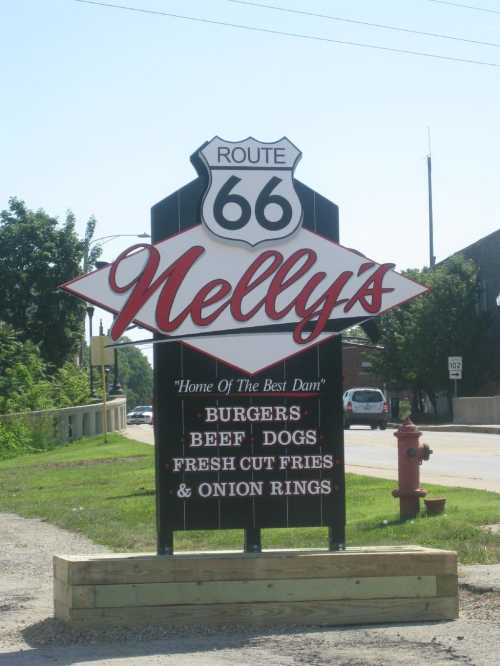 Sign for Nelly's on Route 66, advertising burgers, beef dogs, fresh cut fries, and onion rings.