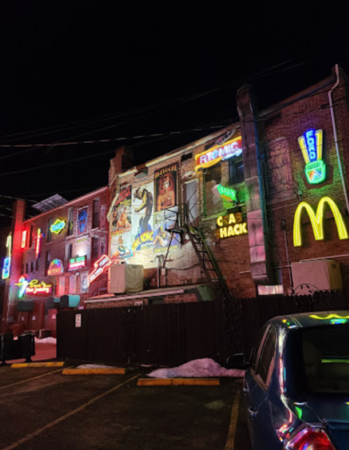 Colorful neon signs illuminate a brick building at night, featuring advertisements and a McDonald's logo.