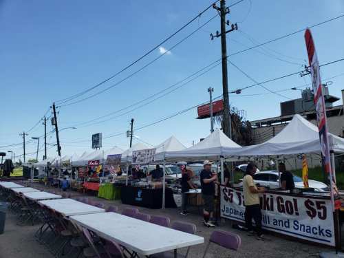 A row of food stalls with tents at an outdoor market, featuring signs for Japanese food and snacks.