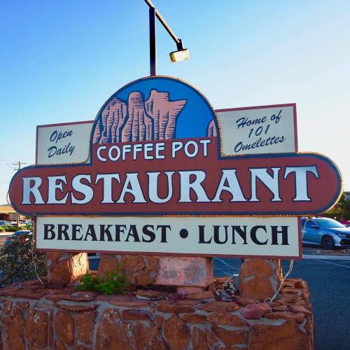 Sign for Coffee Pot Restaurant, featuring "Breakfast" and "Lunch," with a colorful design and stone base. Open daily.