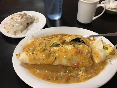A large burrito smothered in cheese and sauce, served with a plate of cinnamon rolls and a cup of coffee.