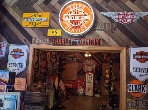 A vintage garage filled with Harley-Davidson memorabilia, signs, and a glowing "Sales & Service" neon light.