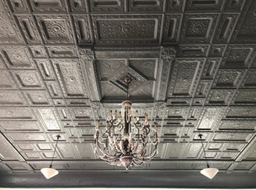 Ornate ceiling with intricate patterns and a vintage chandelier in the center, illuminated by two pendant lights.