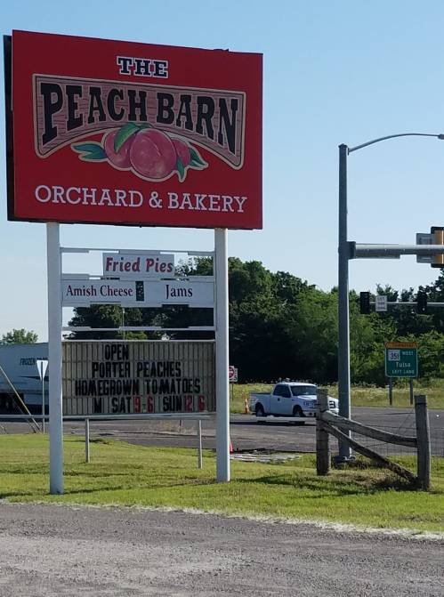 Sign for "The Peach Barn Orchard & Bakery" featuring fried pies, jams, and open hours for peaches and tomatoes.