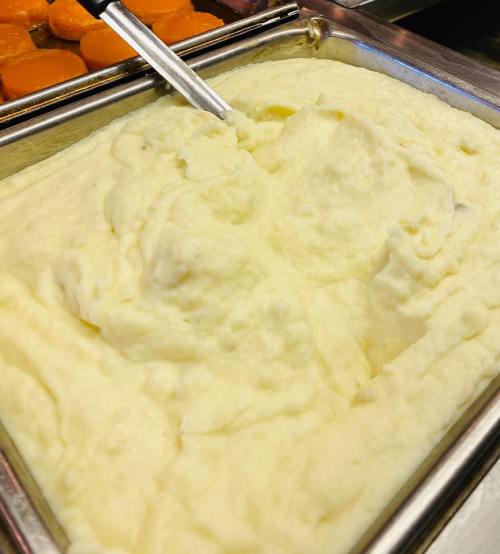A metal tray filled with creamy mashed potatoes, with a serving spoon resting on top.
