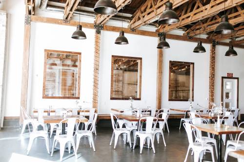 Bright, modern dining space with wooden beams, white walls, and metal chairs arranged around wooden tables.