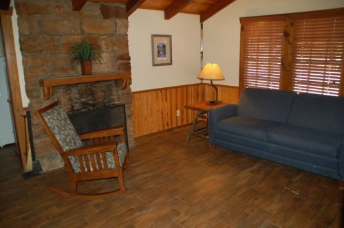 Cozy living room with a stone fireplace, wooden accents, a blue couch, rocking chair, and a lamp.