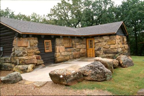 A rustic stone and wood cabin with a sloped roof, surrounded by large rocks and greenery.