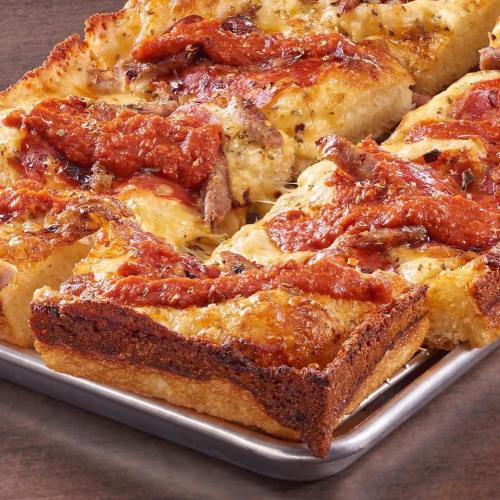 A close-up of a golden-brown, cheesy pizza topped with pepperoni and sauce, served on a metal tray.