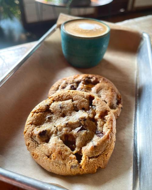 A tray with two chocolate chip cookies and a small cup of espresso on a wooden table.