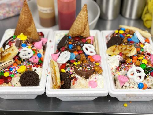 Three large ice cream sundaes topped with colorful candies, sprinkles, cookies, and waffle cone pieces.