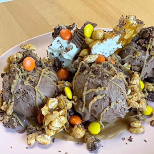 A plate of chocolate ice cream scoops topped with caramel, candy pieces, and crunchy toppings.