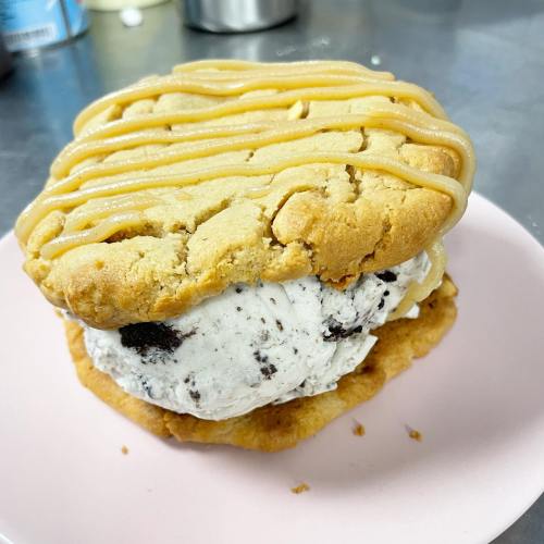 A large cookie sandwich filled with cookies and cream ice cream, topped with a drizzle of caramel.