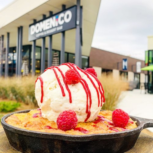 A warm dessert in a skillet topped with ice cream, raspberries, and drizzled with red sauce, outside a restaurant.