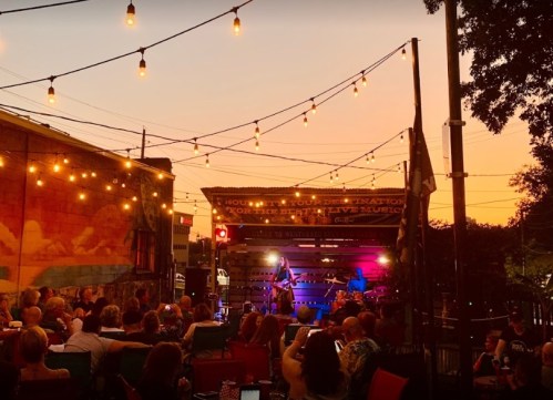 A lively outdoor music performance at sunset, with string lights illuminating a crowd enjoying the show.