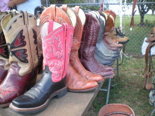 A row of colorful cowboy boots displayed on a table outdoors, featuring various styles and designs.