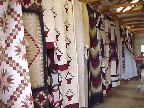 A display of colorful quilts hanging on a wall in a spacious indoor setting.