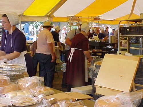 A bustling outdoor market with vendors in traditional attire preparing and selling baked goods under a yellow-striped tent.