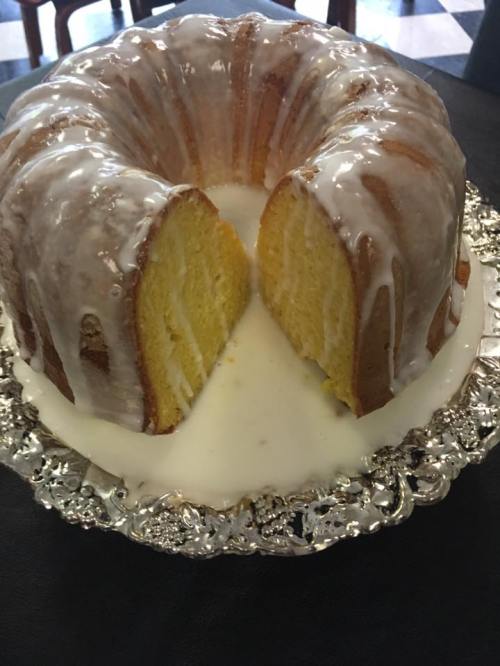 A glazed bundt cake on a silver platter, with a slice cut out, revealing its moist yellow interior.