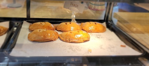 Five golden-brown peach pastries displayed in a bakery case, labeled "Peach."