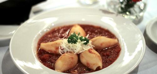 A plate of stuffed pasta shells in marinara sauce, garnished with parsley and shredded cheese.