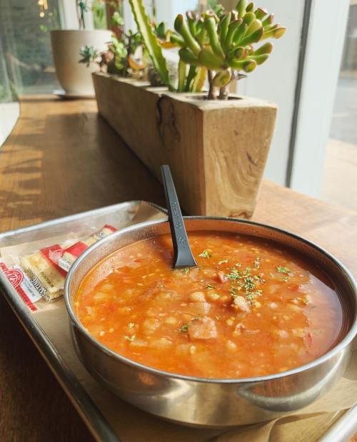 A bowl of soup with beans and herbs, served on a tray with crackers, beside a planter of succulents.