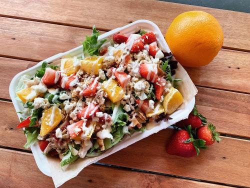 A colorful salad with lettuce, strawberries, oranges, and chicken, served in a tray, alongside an orange and strawberries.