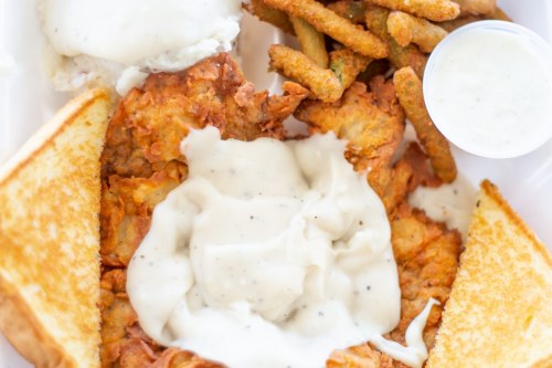 A plate of fried chicken smothered in gravy, served with toast, green beans, and a side of ranch dressing.