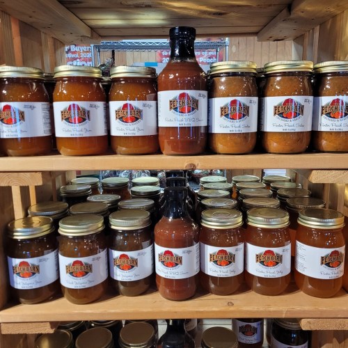 A wooden shelf displaying various jars of peach preserves and sauces, labeled with "Peach Bran."