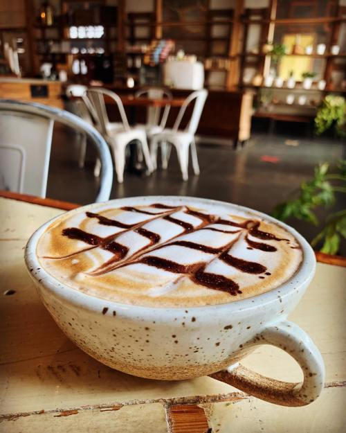 A close-up of a latte in a speckled ceramic cup, topped with chocolate drizzle, set on a rustic wooden table.