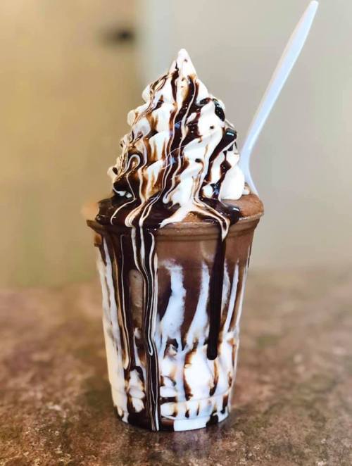 A delicious ice cream cup with swirls of chocolate and vanilla, topped with chocolate drizzle and a spoon.