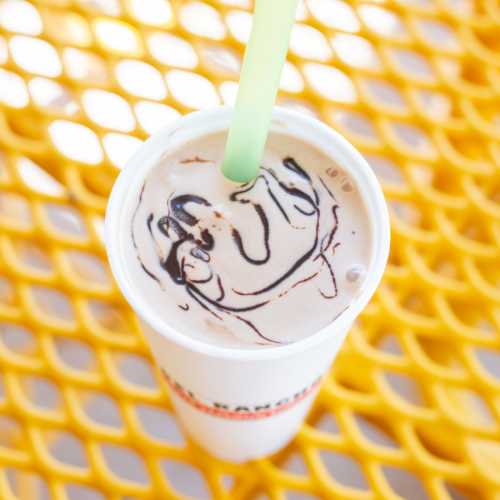 A cup of chocolate swirl drink with a green straw on a yellow table.