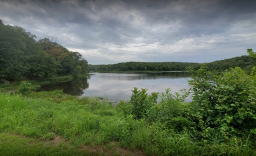 A serene lake surrounded by lush greenery under a cloudy sky.