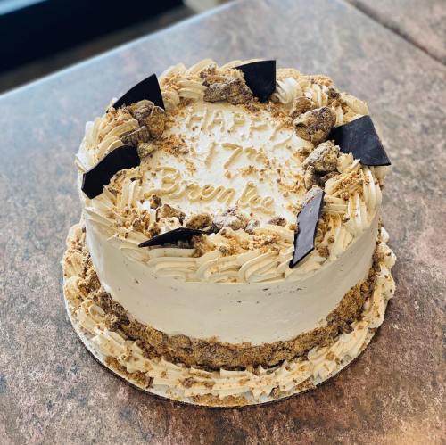 A round cake decorated with cream, chocolate pieces, and a "Happy 7th Birthday" inscription on top.