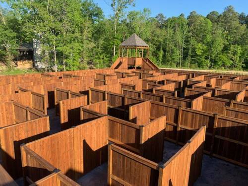 Aerial view of a large wooden maze surrounded by trees, with a lookout tower in the center.