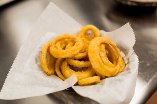 A basket of golden, crispy onion rings on a white paper liner.