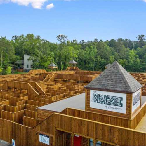 Aerial view of a large wooden maze surrounded by trees, featuring a tower with "The Maze" sign.