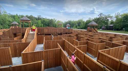 Aerial view of a large wooden maze with several people exploring its pathways under a blue sky.