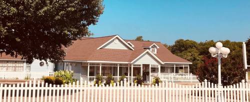 A charming blue house with a brown roof, surrounded by a white picket fence and lush greenery under a clear blue sky.