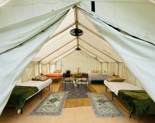 Interior of a spacious tent with beds, a table, and decorative rugs, creating a cozy, inviting atmosphere.