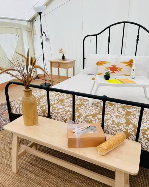 Cozy tent interior featuring a bed, wooden bench, decorative vase, and a small table with items on it.