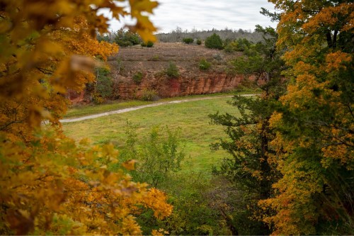 A scenic view of a grassy field bordered by trees with autumn foliage and a rocky hillside in the background.