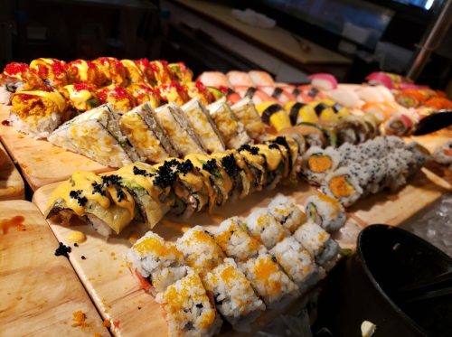 A colorful assortment of sushi rolls displayed on a wooden platter, featuring various toppings and styles.