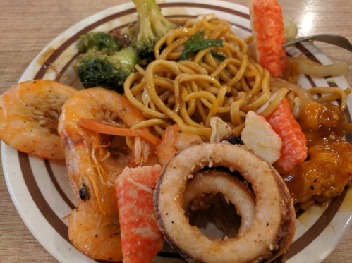 A plate of mixed seafood including shrimp, crab, and squid, served with broccoli and lo mein noodles.