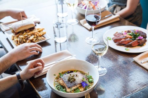 A table set with various dishes, including salmon, steak, fries, and drinks, showcasing a vibrant dining experience.
