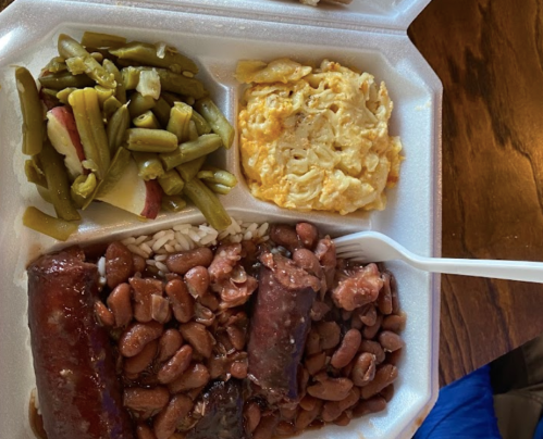 A takeout container with rice, beans, sausage, green beans, and scrambled eggs.
