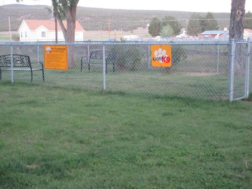 A fenced area with benches and signs, surrounded by grass and trees, in a rural setting.